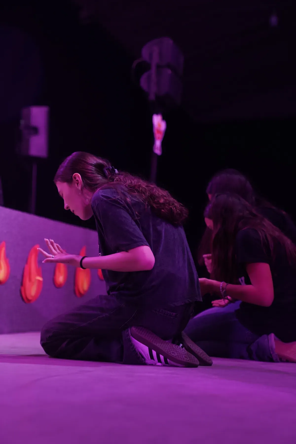 Una chica con la mano en alto durante un momento de adoración, con luces cálidas de fondo.